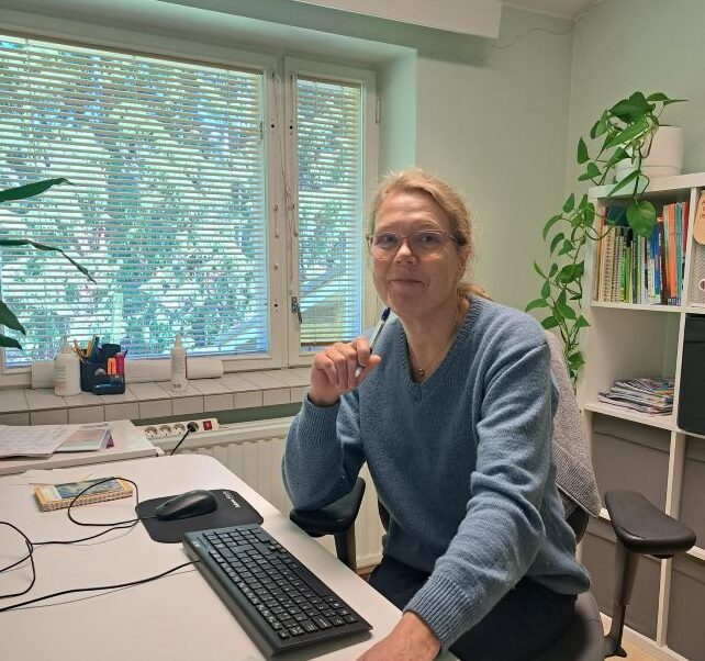 opintovalmentaja istuu työpöydän ääressä, takana viherkasvi